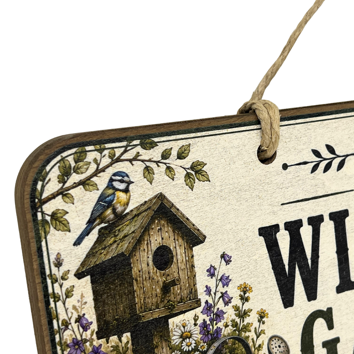 A close-up of a decorative hanging sign with a birdhouse illustration, a bluebird perched on the roof, floral details, and partial black lettering on a cream background. The sign is shown against a white background with part of a rope hanger visible.