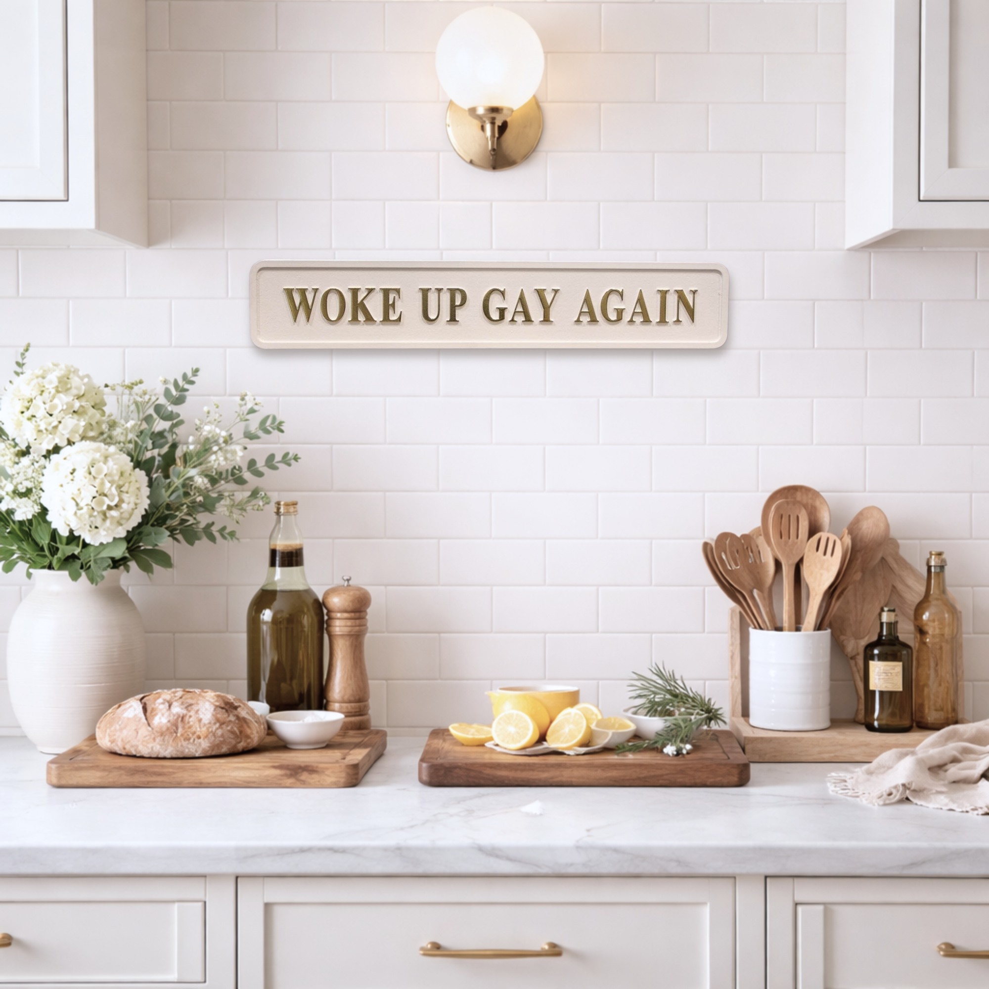 Kitchen counter with decorative sign reading 'WOKE UP GAY AGAIN', flowers, and kitchen utensils.