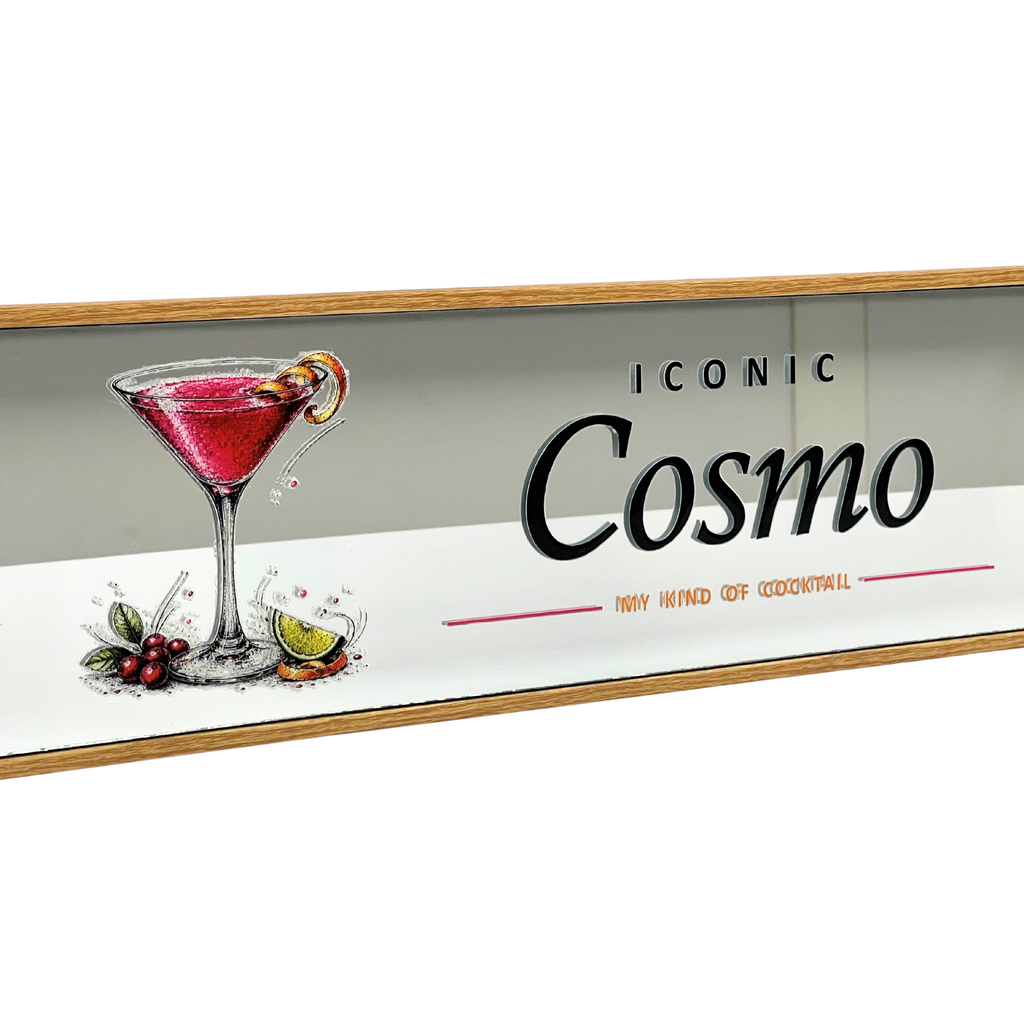 A rectangular bar sign featuring an illustration of a pink martini cocktail with a lime wheel and garnish, alongside the text 'ICONIC Cosmo' and 'THE KIND OF COCKTAIL!' on a white background with a wood-toned border.